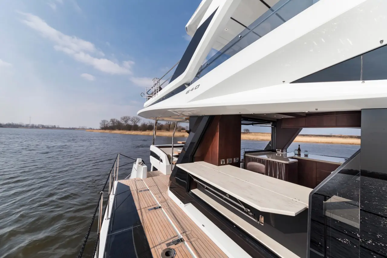 Stylish yacht with a wooden deck, an outdoor dining area, and panoramic views of water and trees under a clear sky.