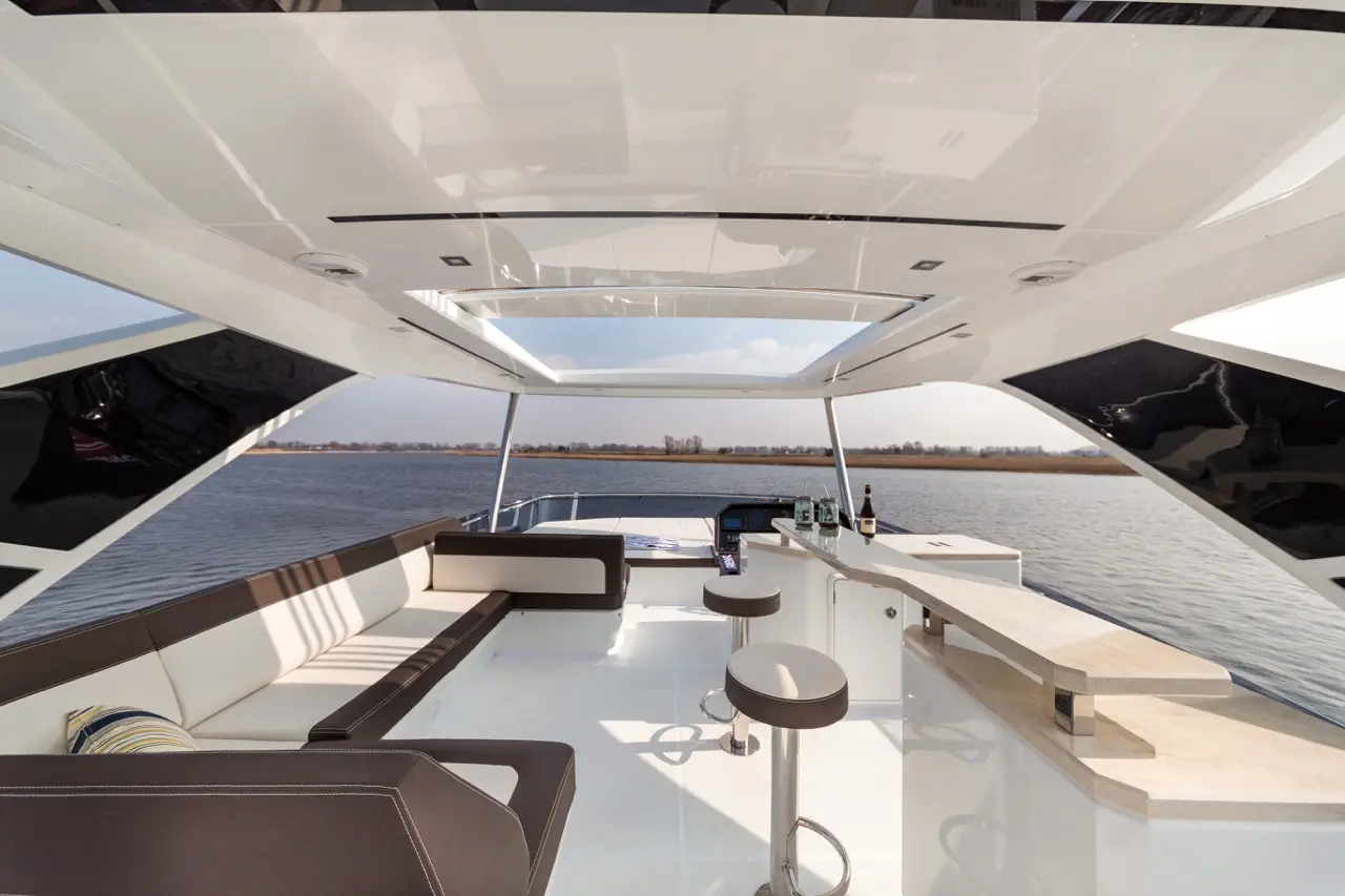 Stylish yacht interior with seating, bar area, and panoramic views of water and shoreline under a bright sky.