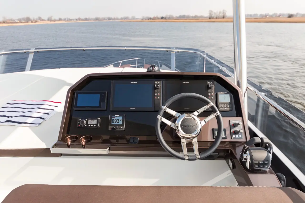 Boat dashboard featuring navigation screens, steering wheel, and communication device, with a striped towel nearby on a sunny day.