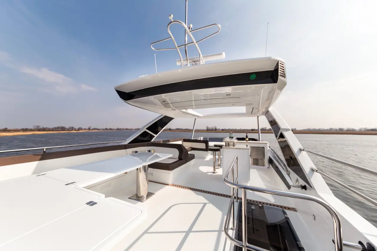 Luxury yacht deck with a spacious seating area, and a helm, overlooking calm waters under a clear sky.