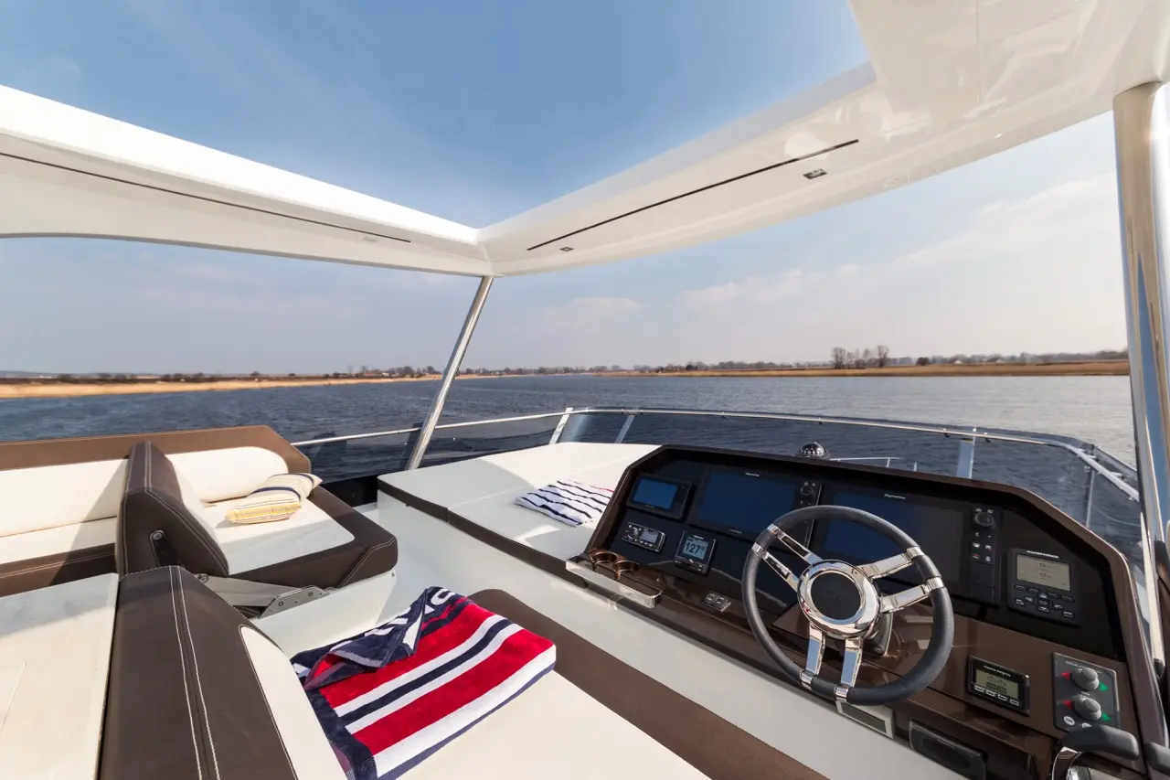 Luxury boat interior displaying a steering wheel, navigational displays, and towels on sun loungers by the water.