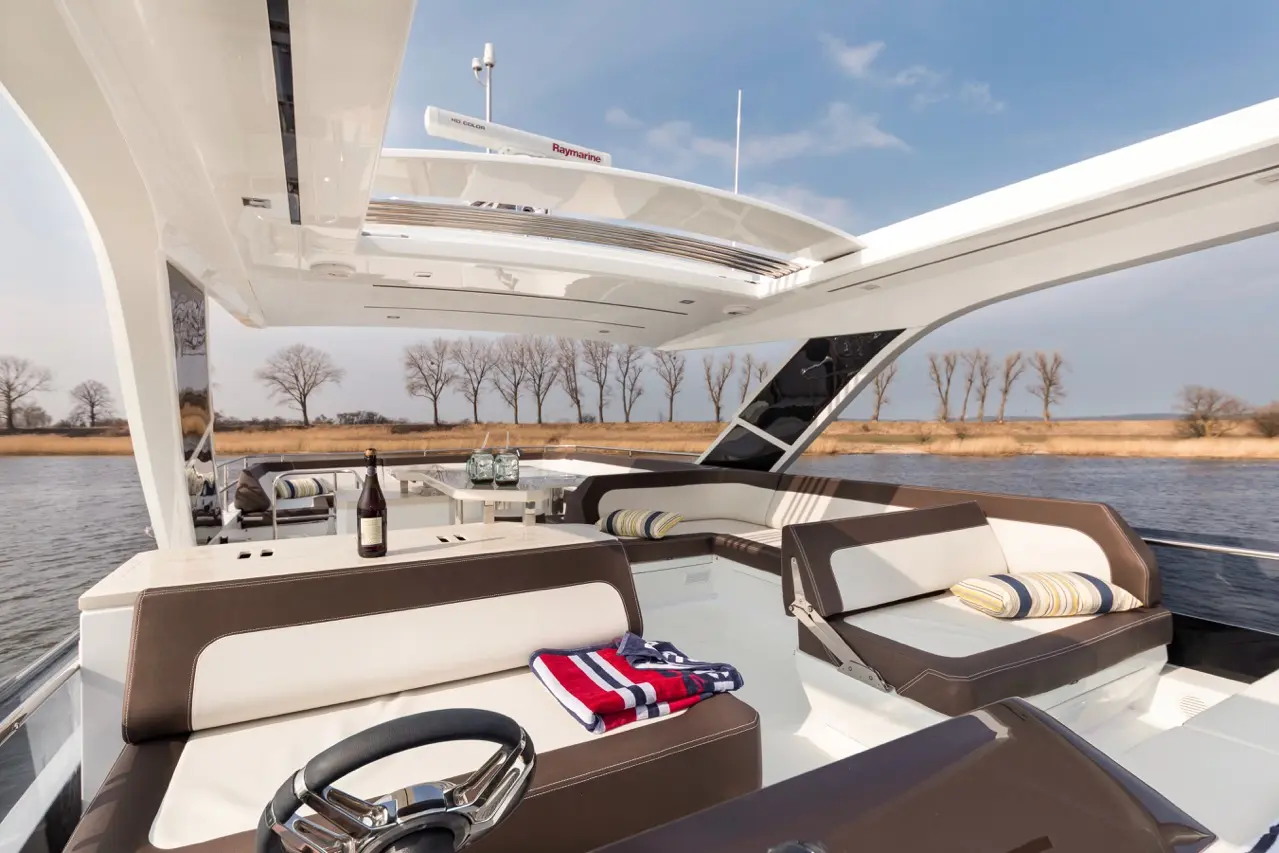 Luxury yacht interior featuring a steering wheel, brown and white seating, a bottle of wine, and river views.