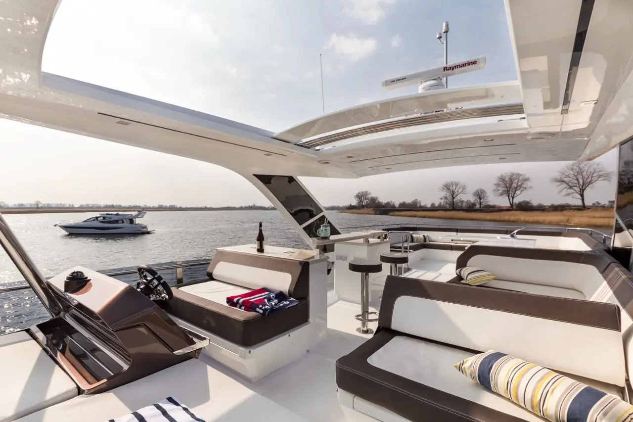 Luxury yacht interior with stylish seating, a steering console, and a view of another boat on the water, under a clear sky.