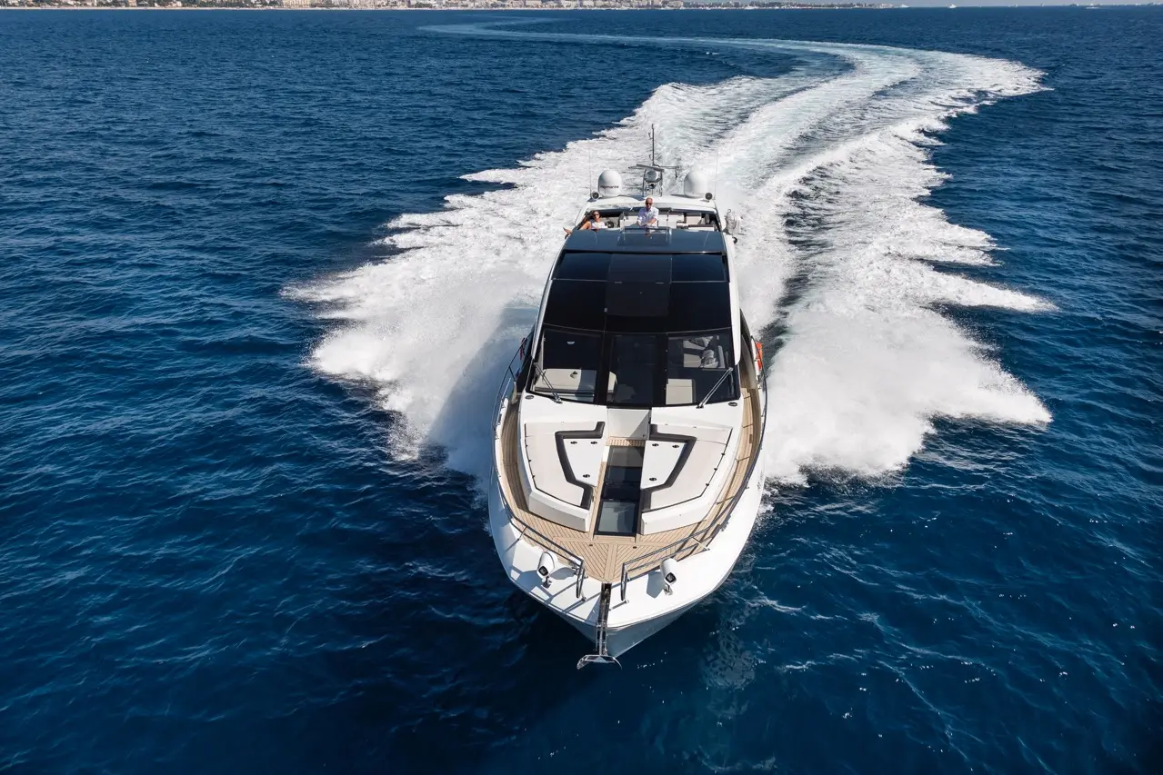 A luxury yacht speeds through deep blue waters, leaving behind a curved wake and capturing a coastal view in the background.