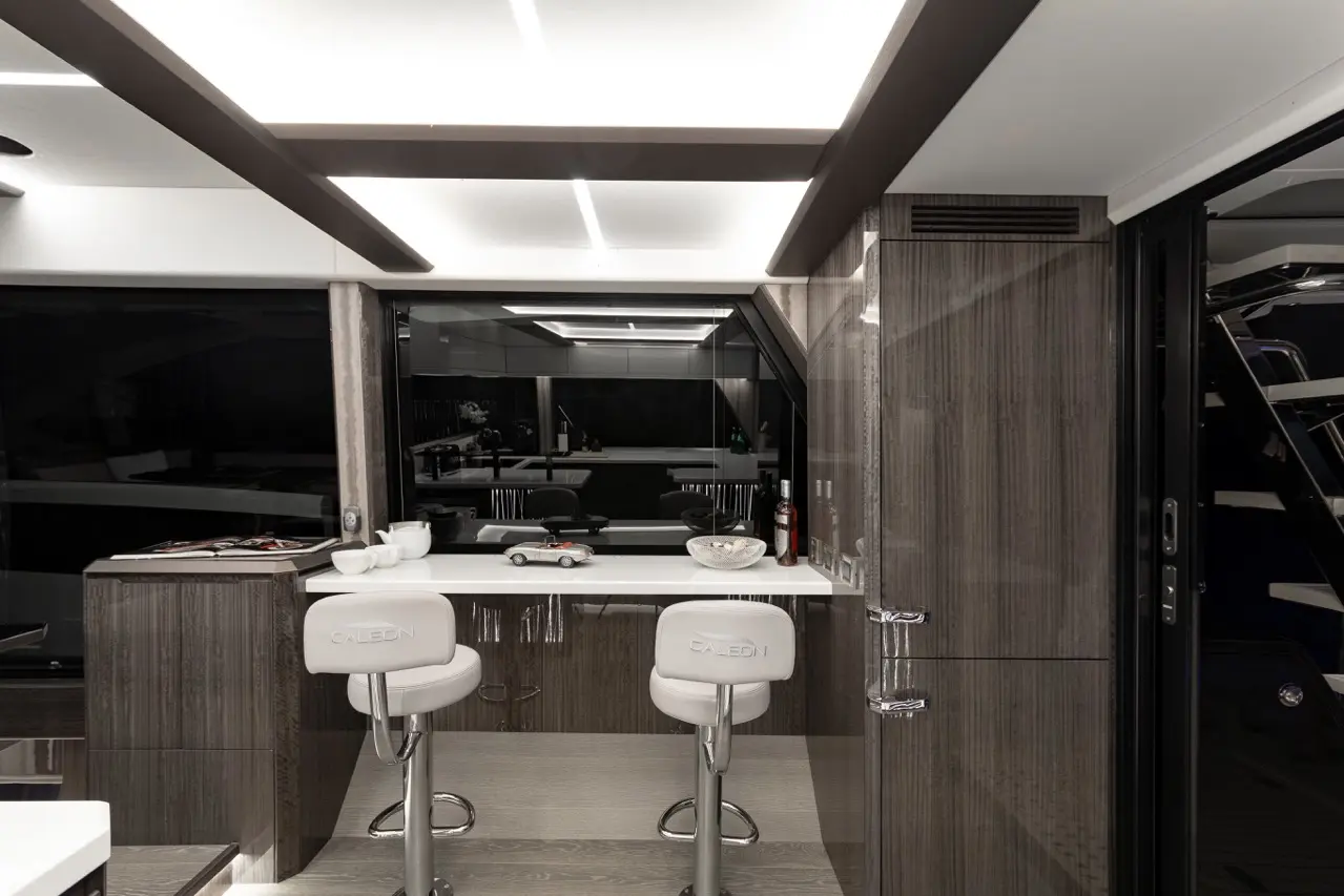 Modern yacht interior with white bar stools, sleek cabinetry, and a panoramic view through large windows.