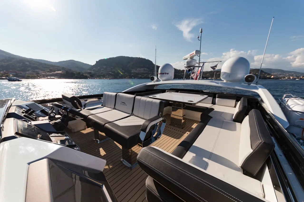 Luxury yacht interior featuring modern seating, cockpit controls, and scenic waterfront view with hills in the background.