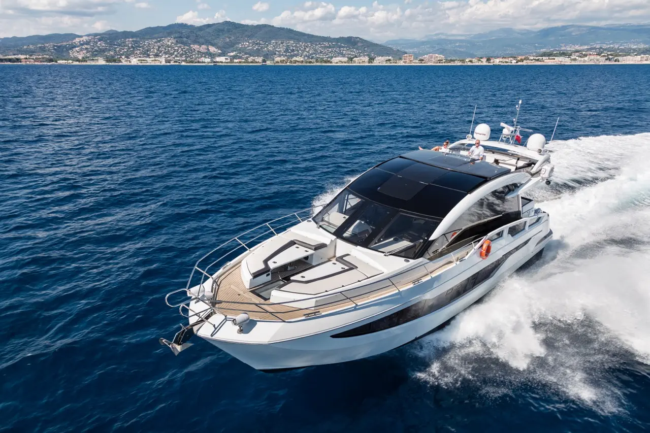 Luxury motor yacht cruising through azure waters with a backdrop of scenic hills and coastline, showcasing modern design features.
