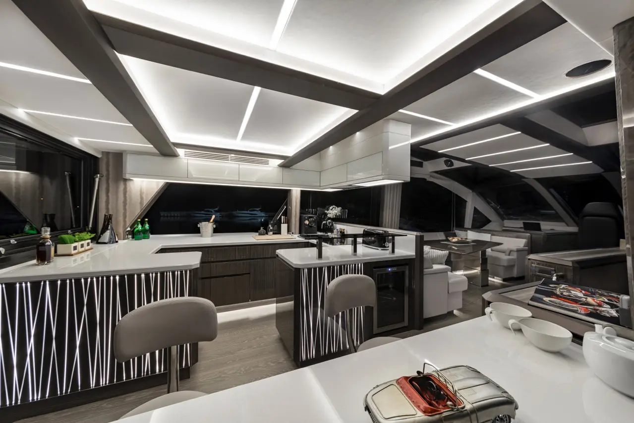 Modern yacht interior featuring sleek kitchen design, illuminated surfaces, and a model car on the table.