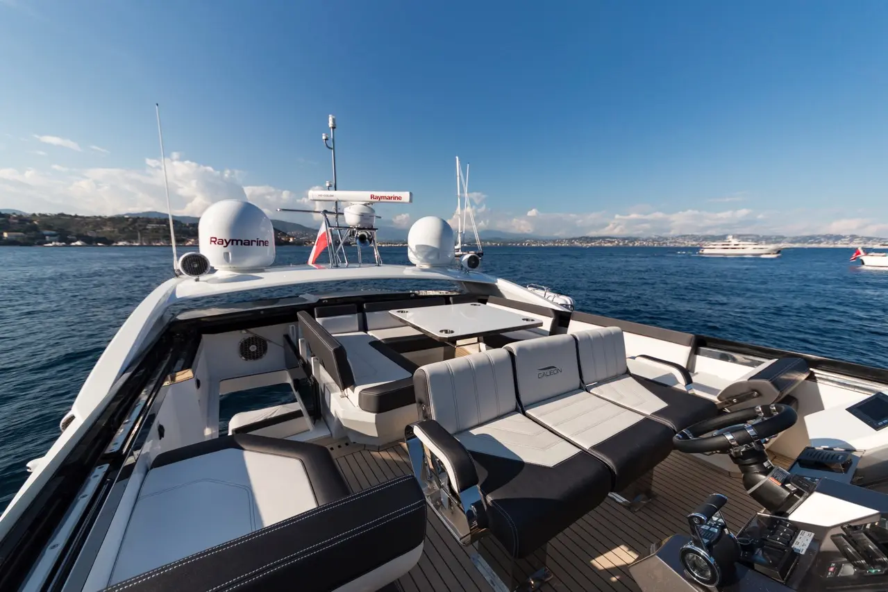Luxury boat deck with grey and black seating, Raymarine equipment, and scenic ocean view under blue skies.