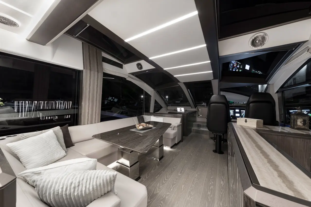 Luxurious yacht interior featuring a spacious lounge with white cushions, dining table, and a helm visible through large windows.