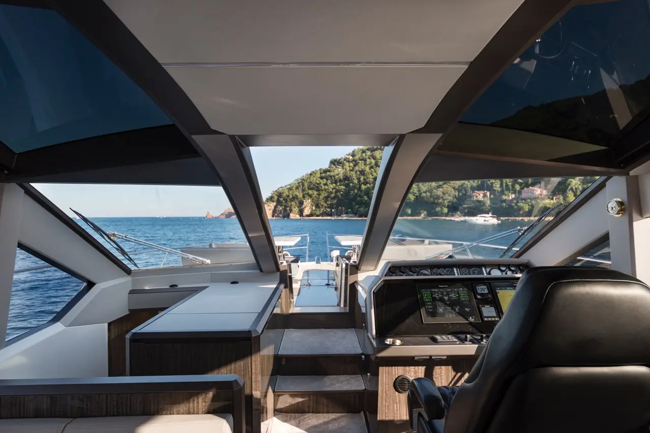 Modern yacht interior featuring a sleek helm, leather seat, and panoramic views of the sea and lush coastline.