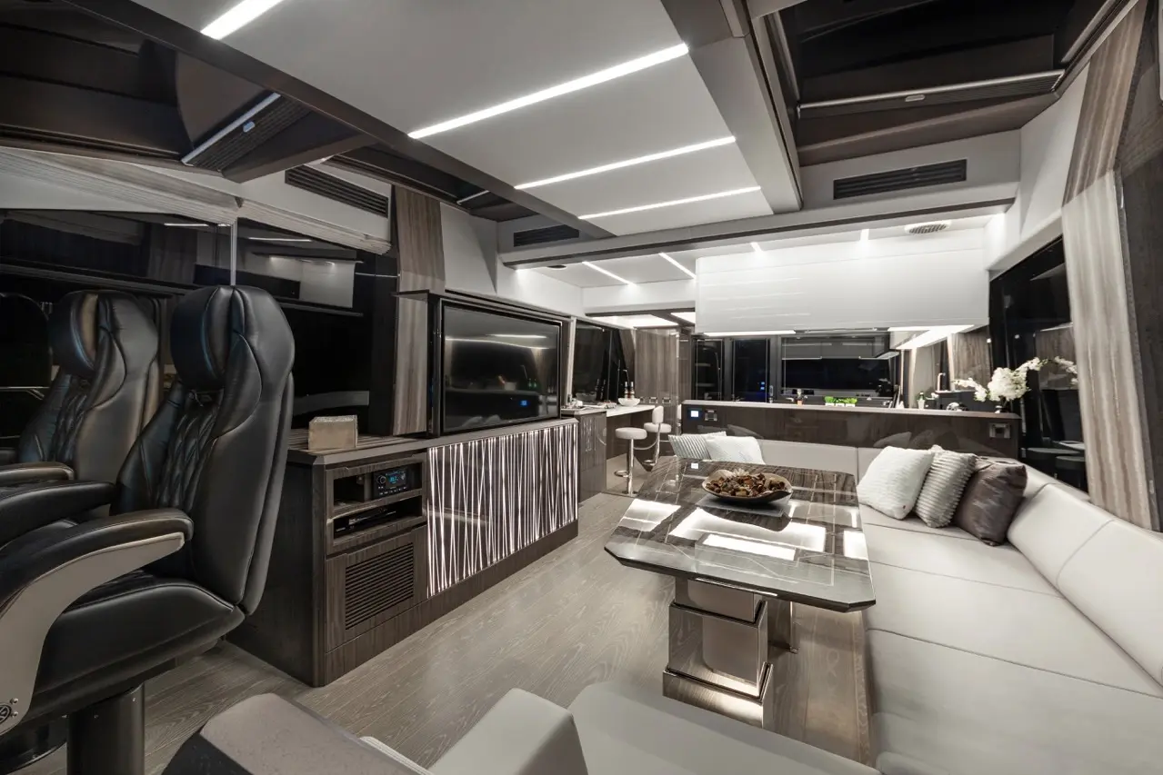 Luxurious interior of a modern RV featuring sleek furnishings, leather seats, large TV, and ambient lighting.