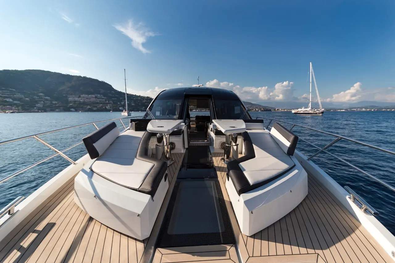 Luxury yacht deck with stylish seating, panoramic views of the sea, and distant hills under a clear blue sky.