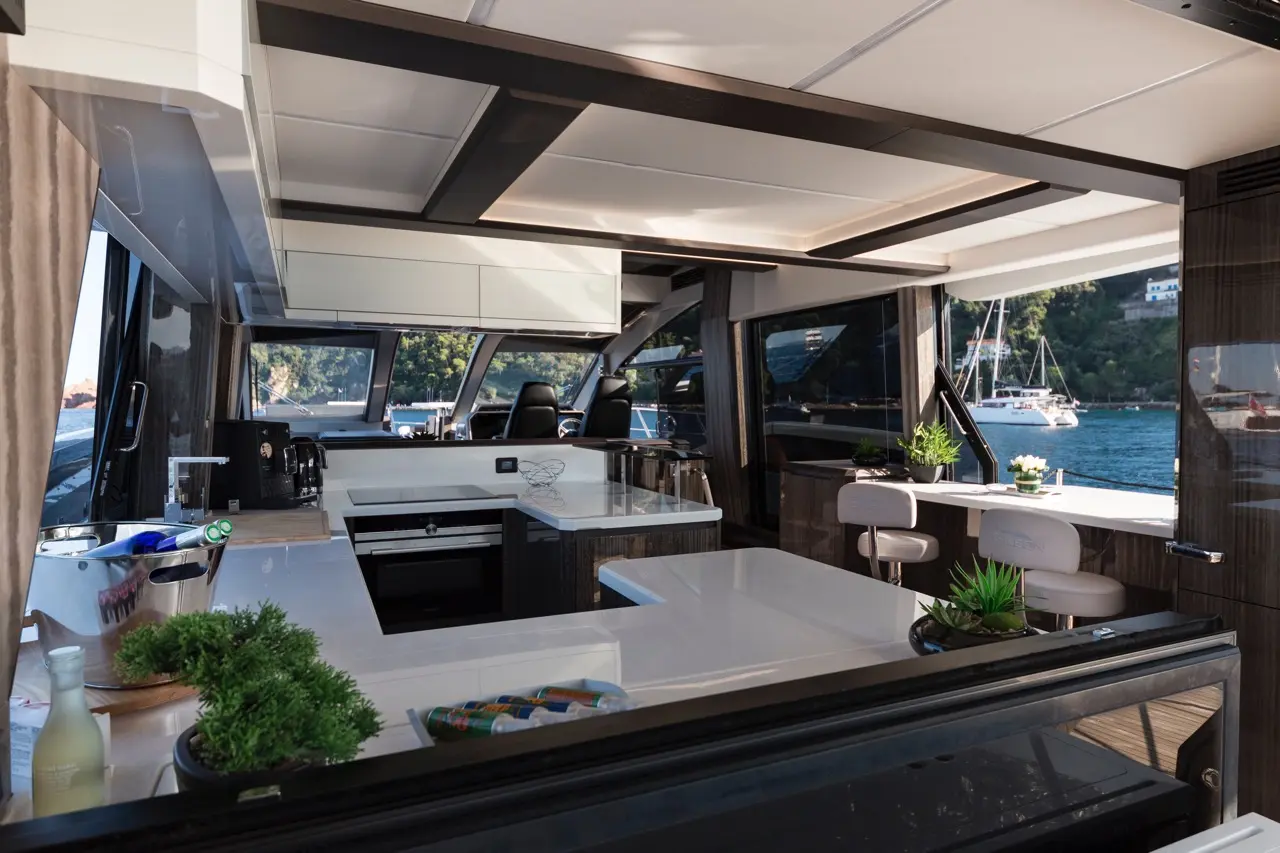 Modern yacht kitchen featuring a white marble countertop, plants, and scenic views of the marina through large windows.
