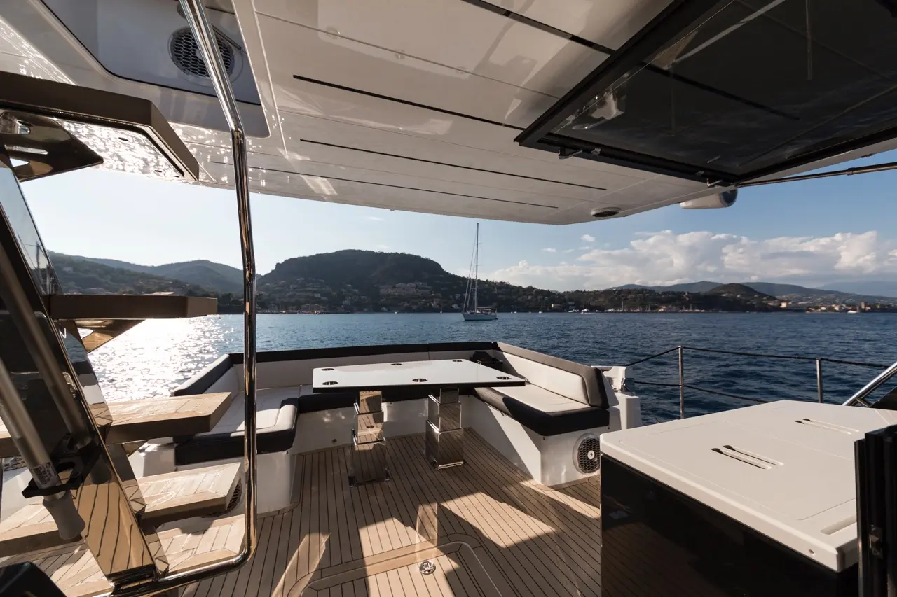 Luxurious yacht deck with a dining area, water view, and mountain backdrop under clear skies. Perfect for relaxation.