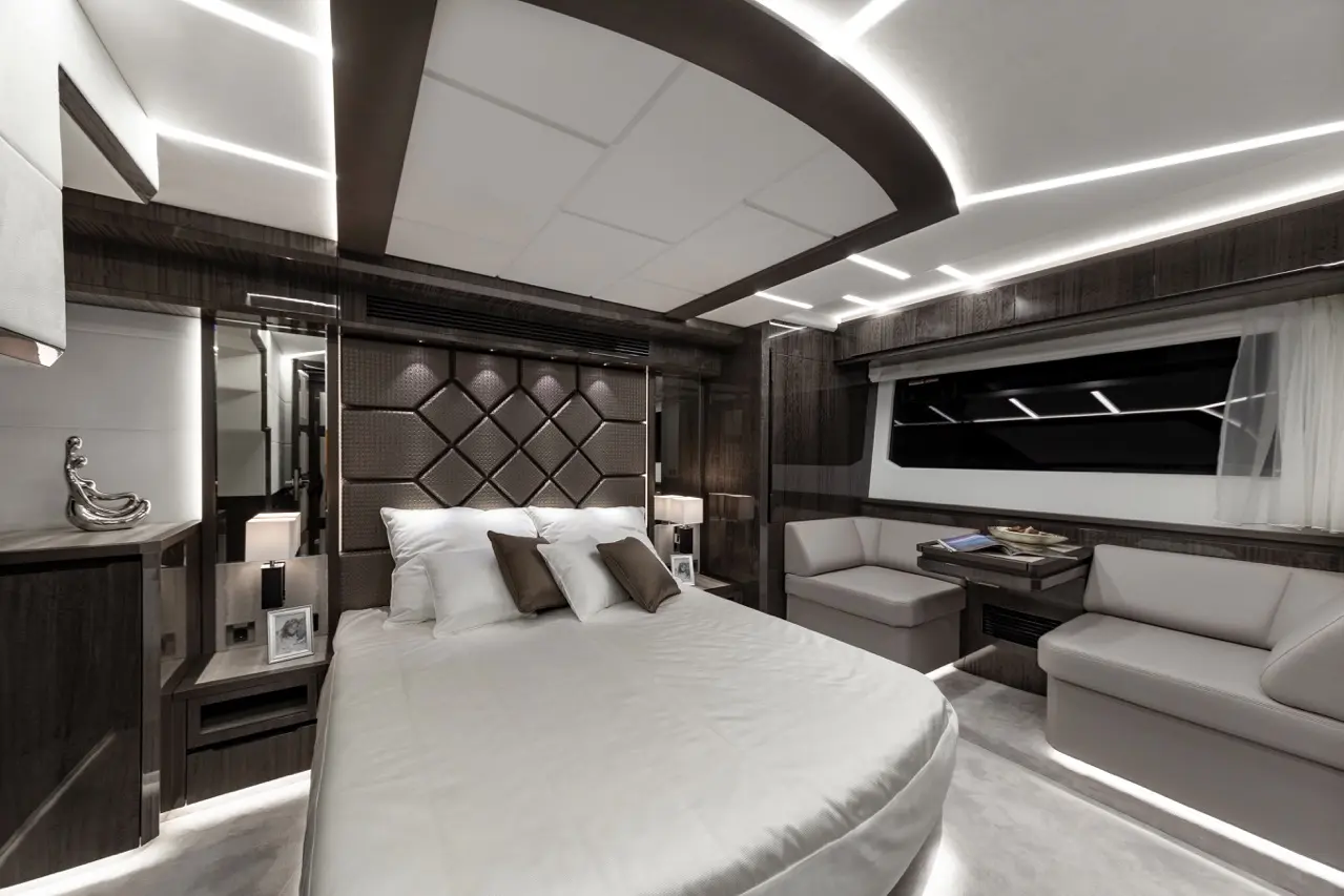 Luxury boat interior featuring a curved bed, modern furnishings, soft lighting, and a seating area by a large window.