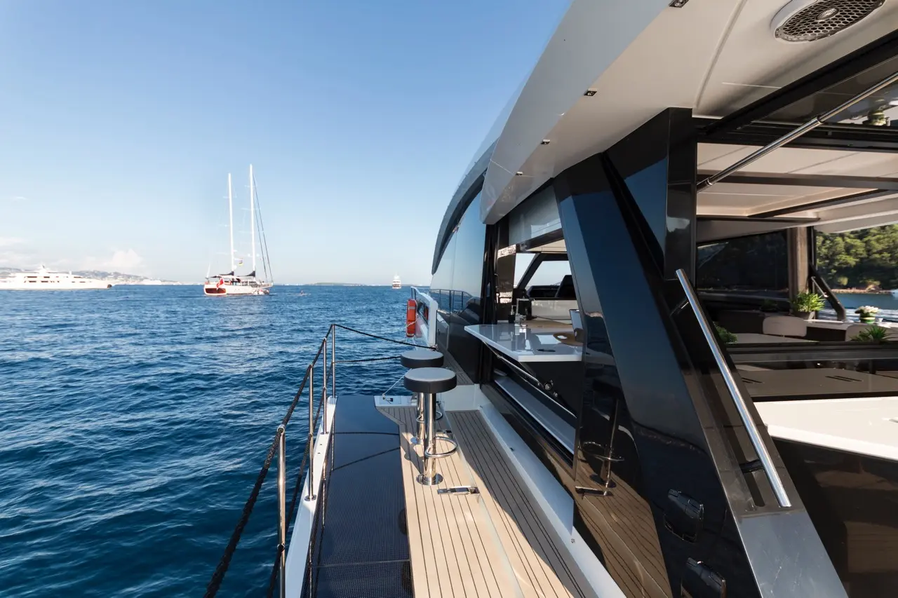 Luxury yacht deck with sleek design, water view, and nearby sailing boats under clear blue sky. Modern outdoor seating visible.