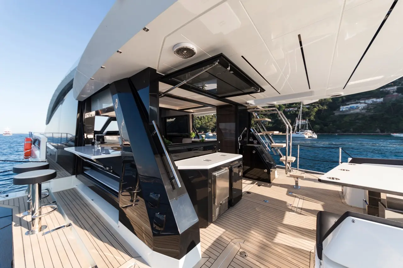 Luxurious yacht deck featuring modern kitchen area, seating, and scenic coastal view with moored boats in the background.