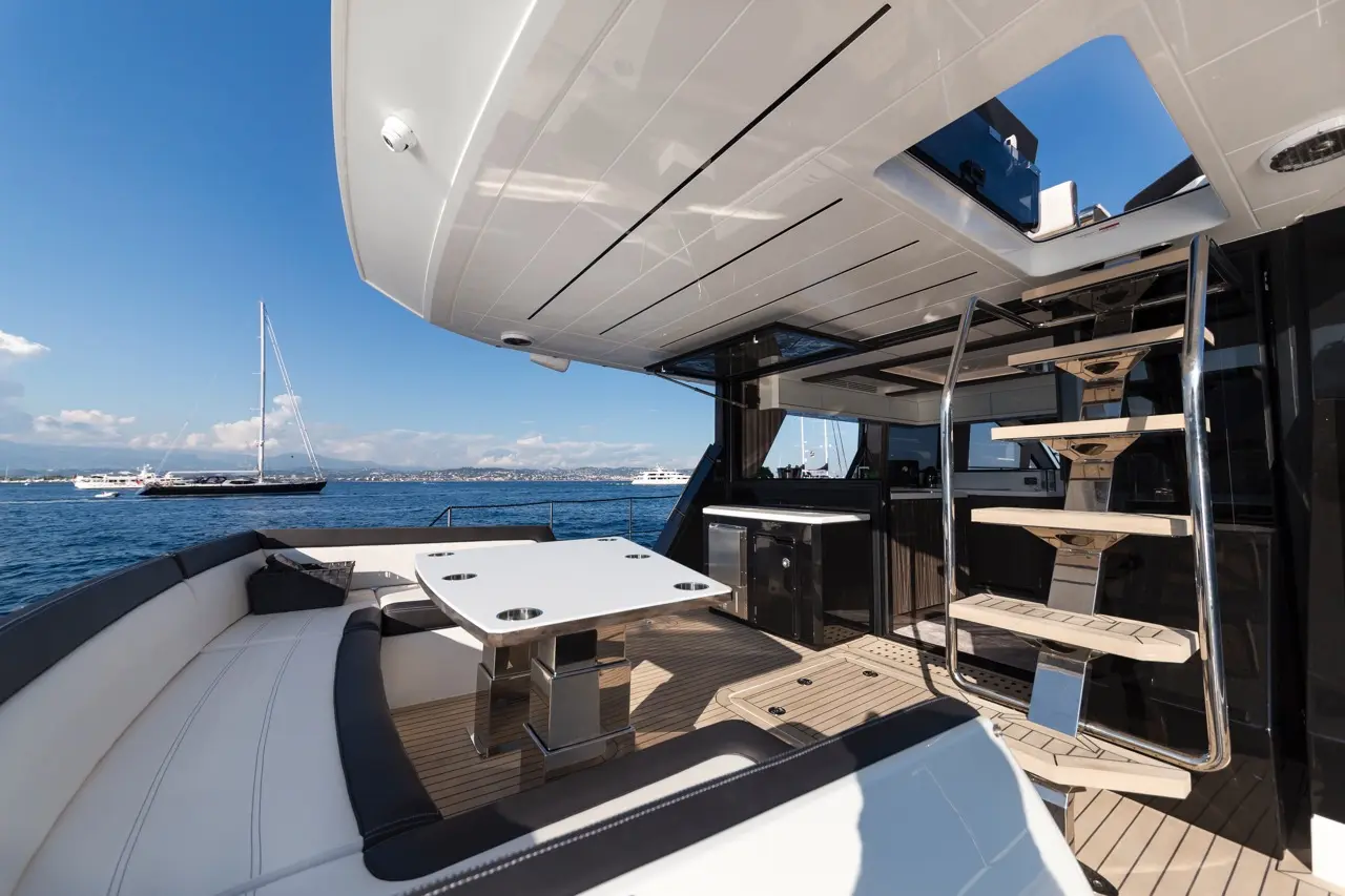 Luxury yacht deck featuring a dining table, a staircase, and stunning sea views with boats in the background.
