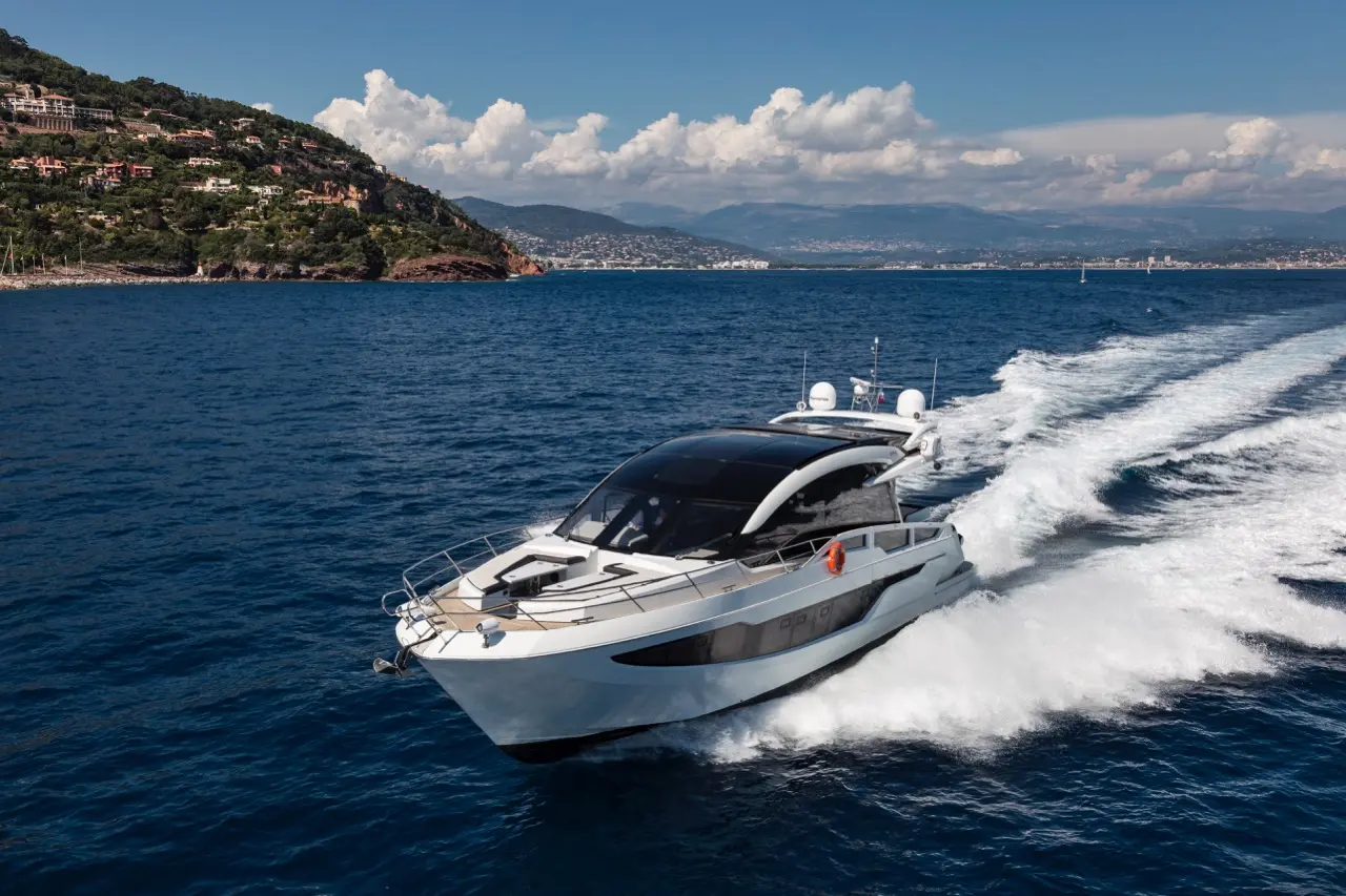 Luxury motor yacht navigating through blue waters with coastal scenery and mountains in the background.