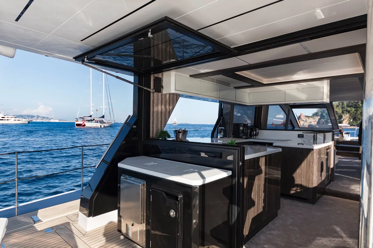 Modern yacht interior featuring an open kitchen with a view of boats on the water and coastal scenery in the background.