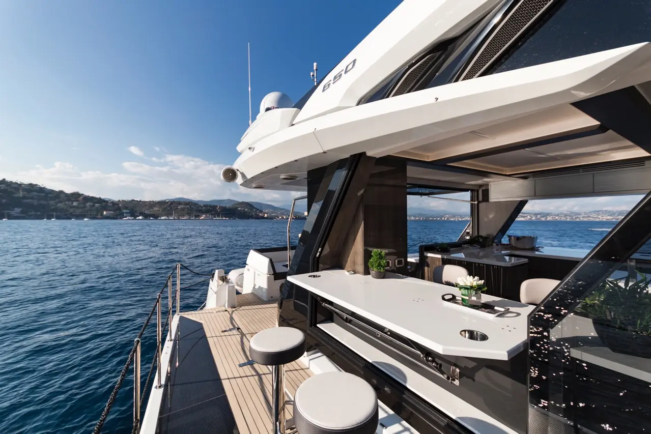 Luxurious yacht deck with modern furniture, overlooking calm blue waters and distant hills under a clear sky.