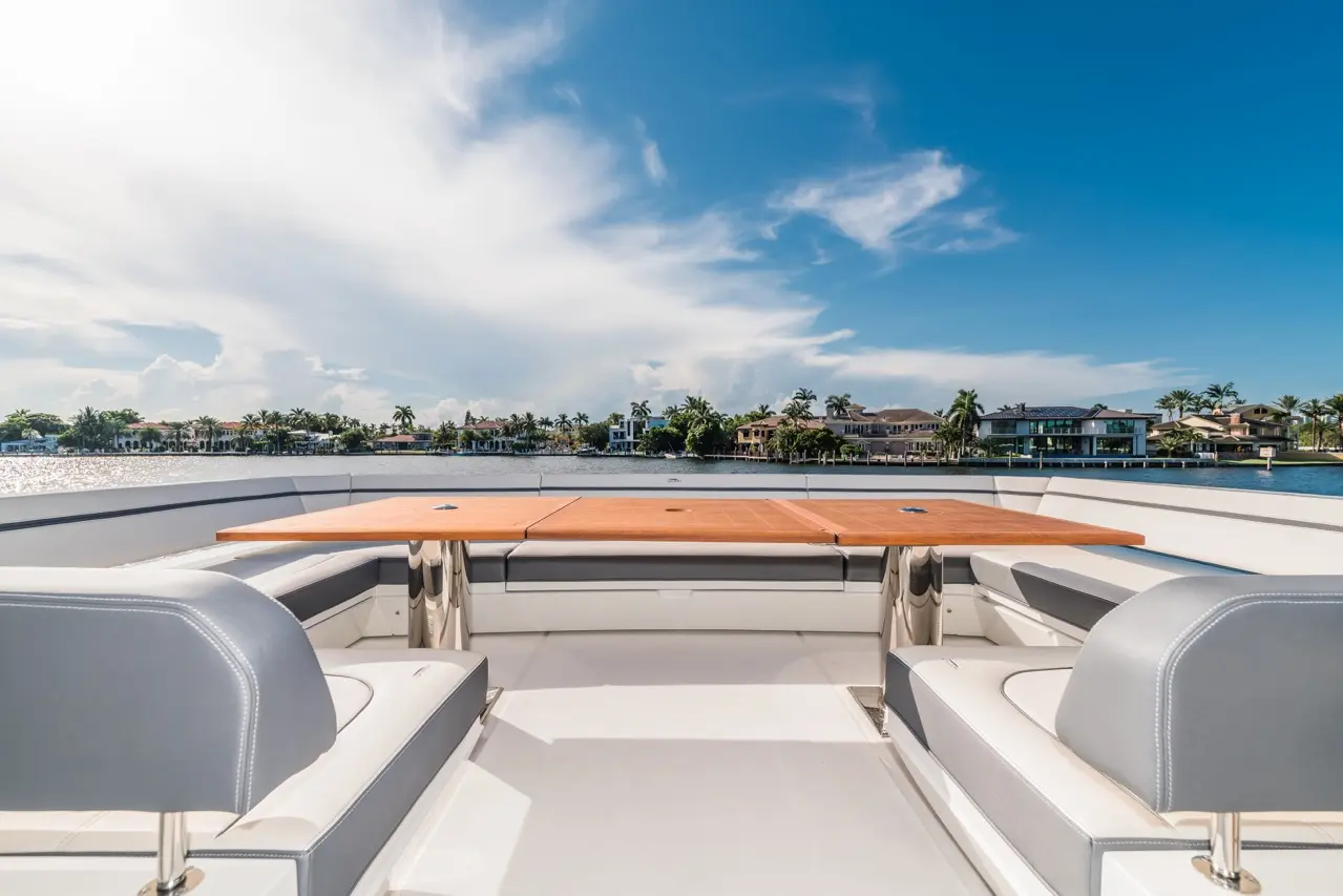 Luxury yacht deck with a wooden table, grey seating, and a view of waterfront homes against a blue sky.