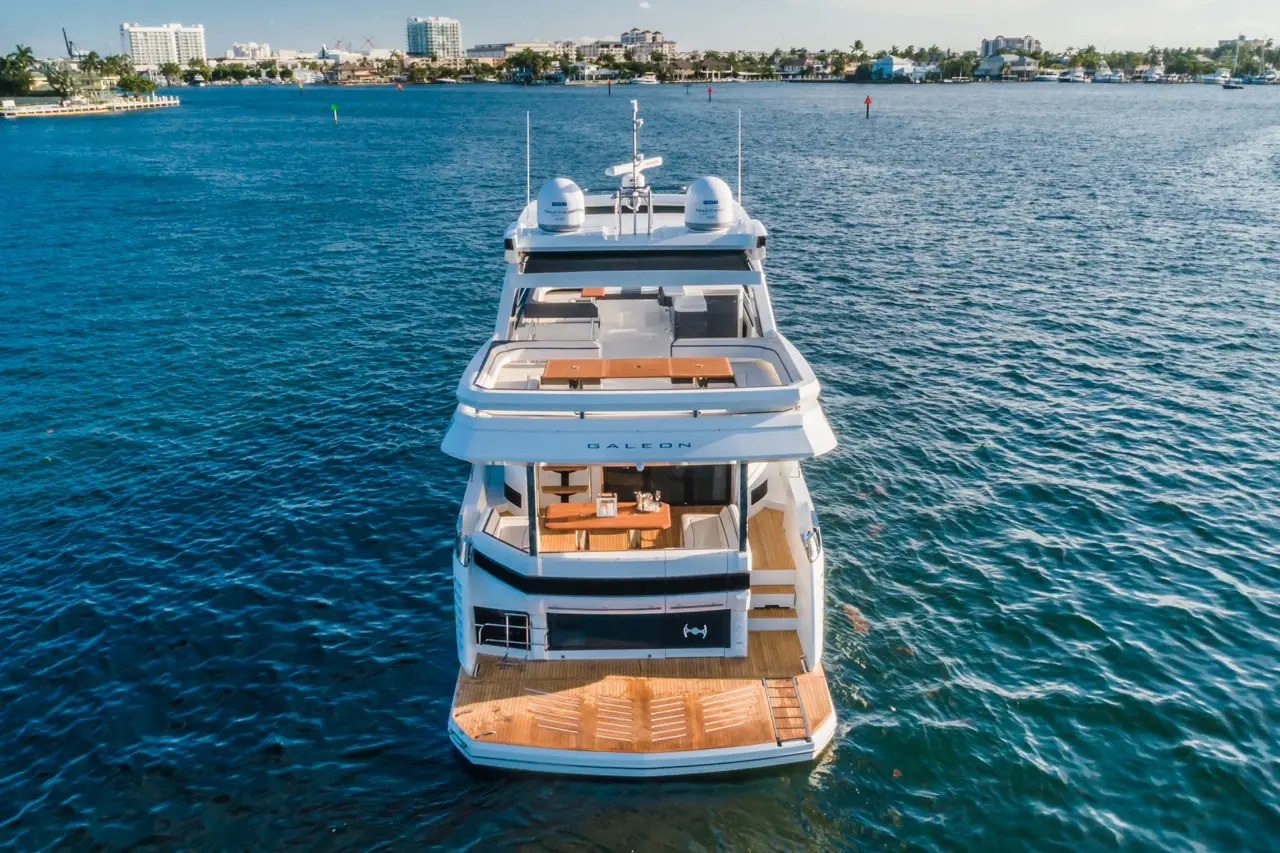 A luxury Galeon yacht moored in clear blue water, showcasing its spacious upper deck and wooden rear platform.