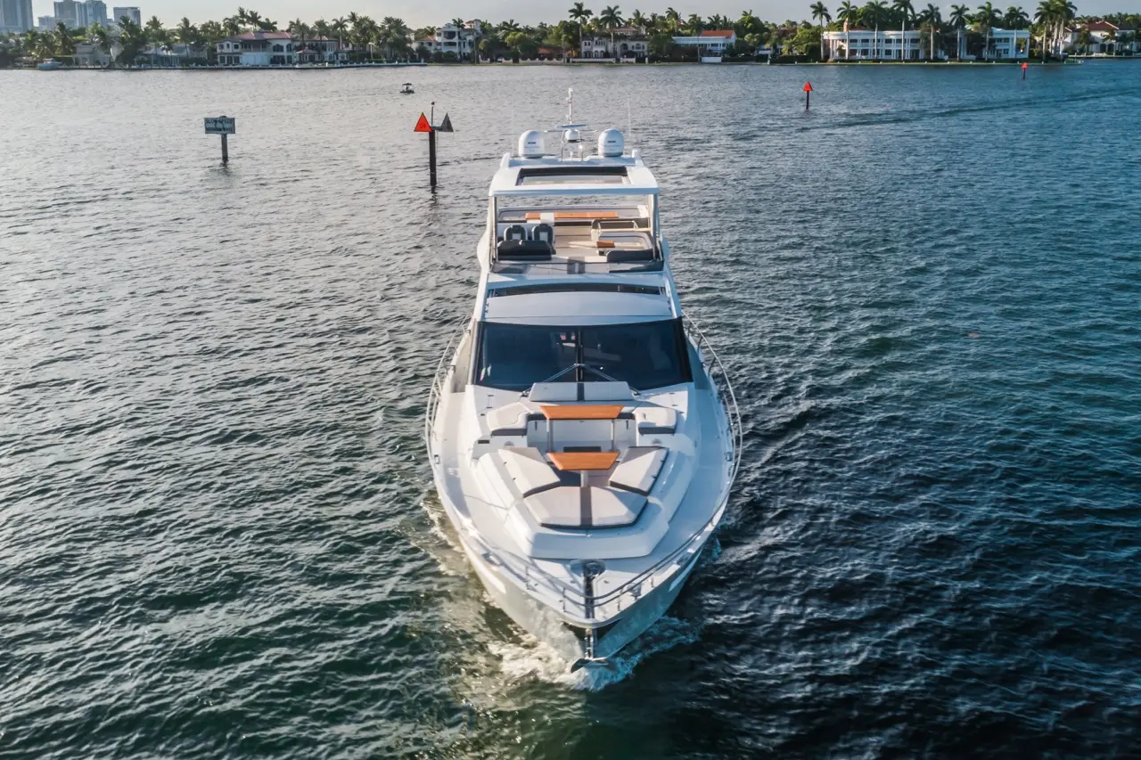 A sleek motorboat navigates through calm waters, with waterfront properties and palm trees in the background.