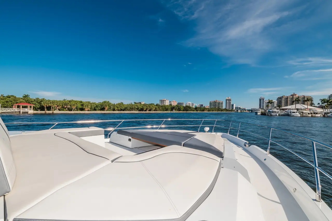 View from the bow of a yacht on a clear day, showcasing blue skies, waterway, and skyline with buildings in the background.