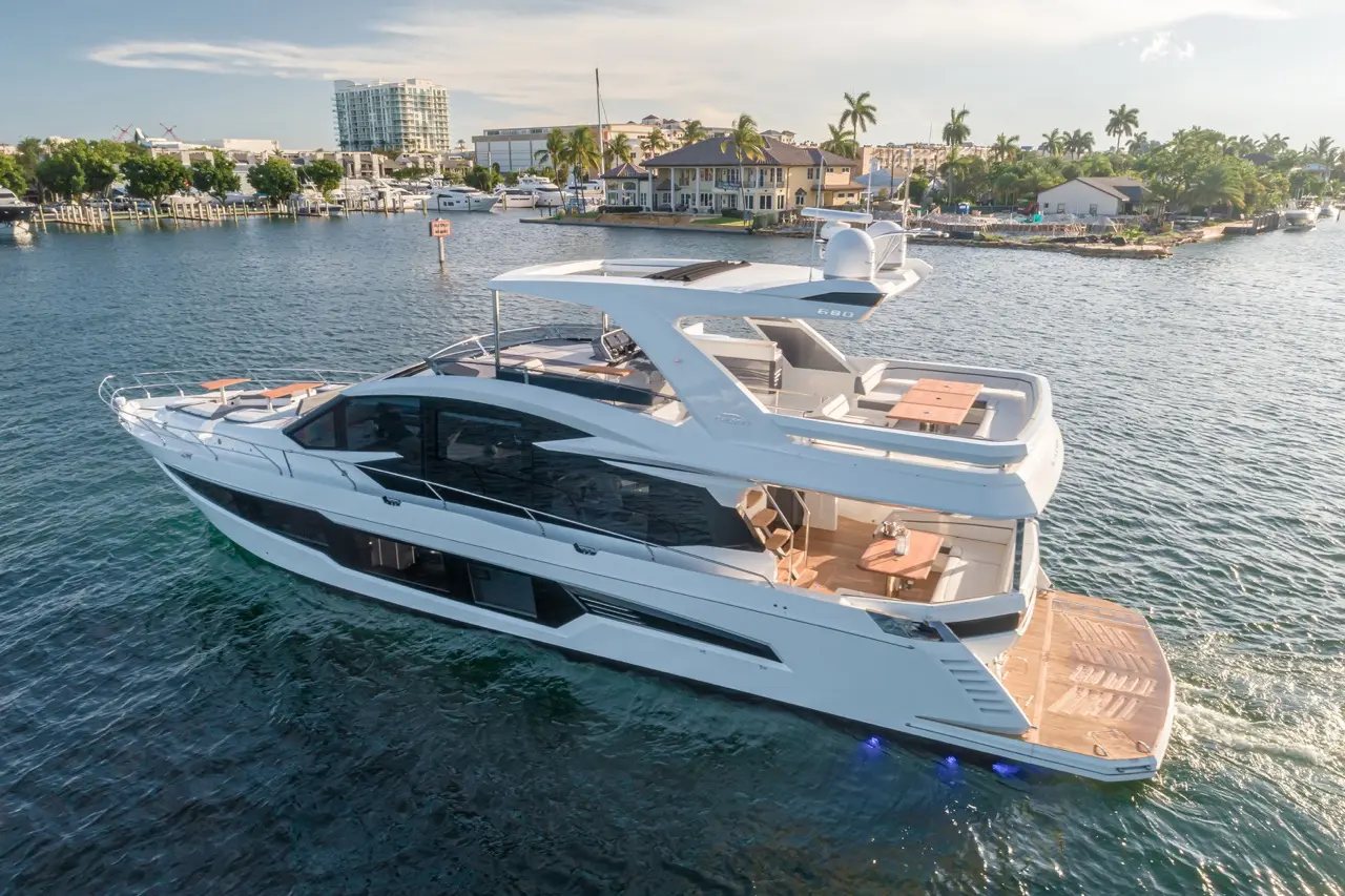 Luxury motor yacht cruising on clear water with modern design, spacious deck, and palm trees lining the shore.