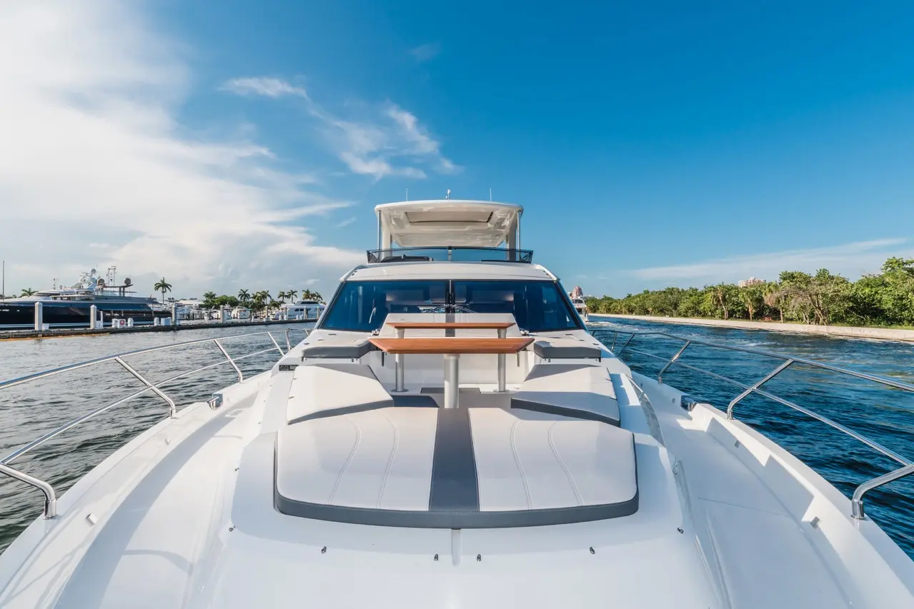 A luxury yacht's bow with a stylish seating area, a table, and a scenic waterfront under a clear blue sky.