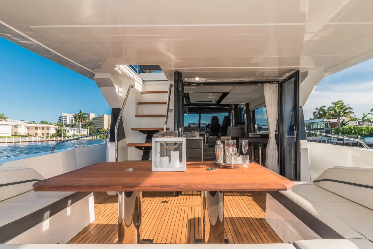 A luxurious yacht interior featuring a polished wooden dining table, glassware, and panoramic views of waterfront properties.