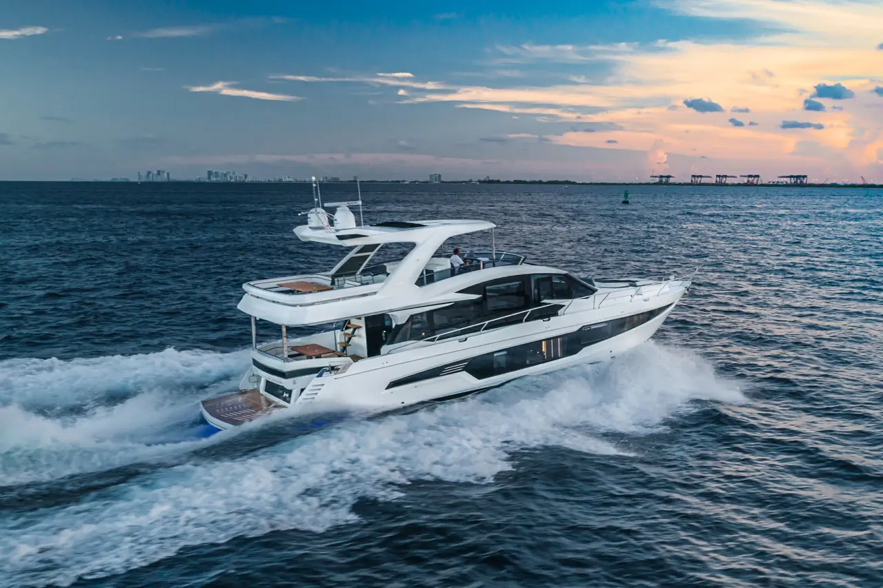 Luxury yacht cruising on water with a city skyline and sunset in the background, showcasing elegance and leisure.