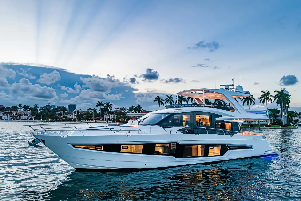 A luxury yacht moored in calm waters, featuring modern designs and twinkling lights, set against a sunset sky with palm trees.