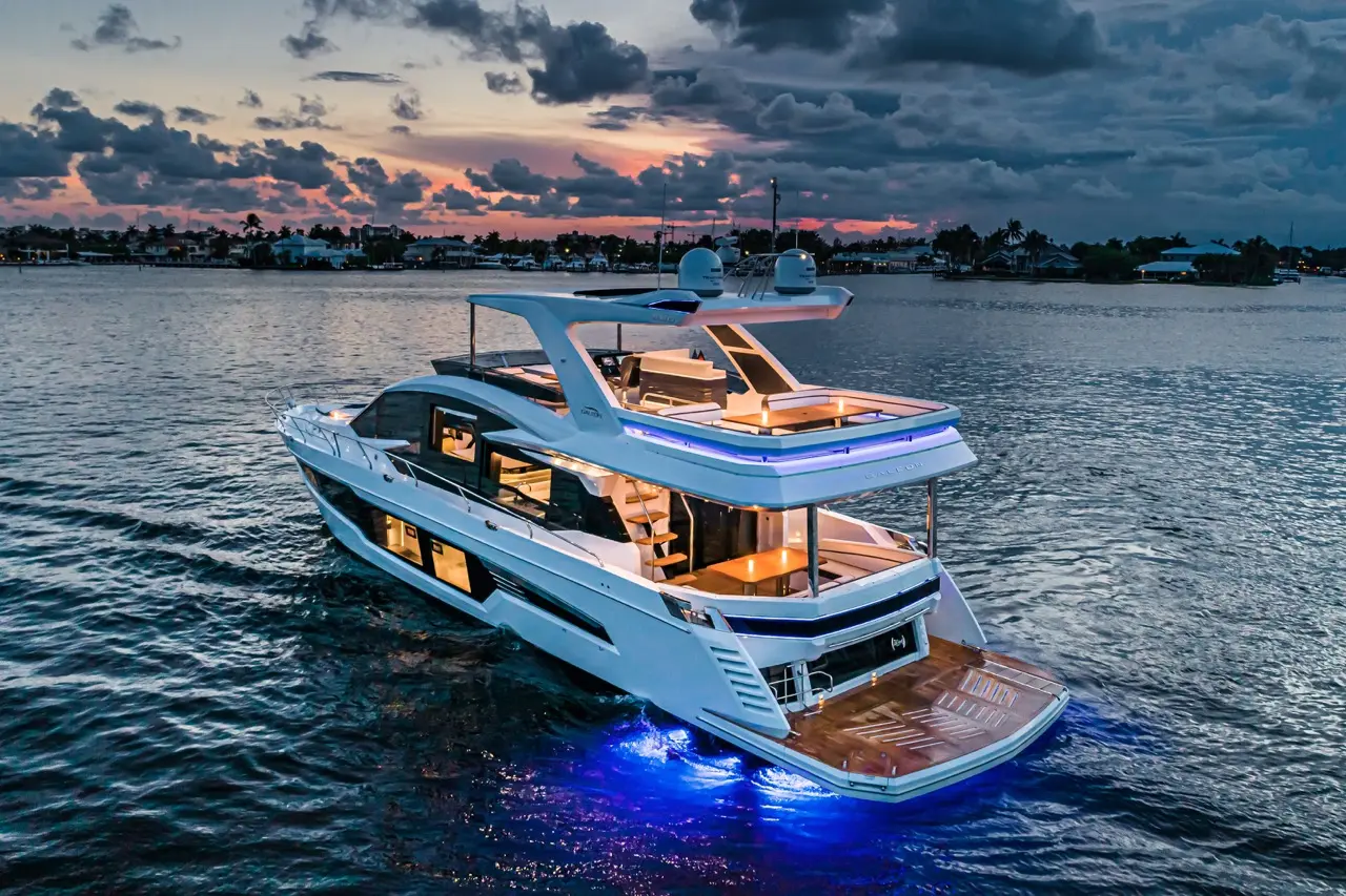 A sleek yacht illuminated with blue lights sailing on calm waters at sunset, showcasing luxury design and sophistication.