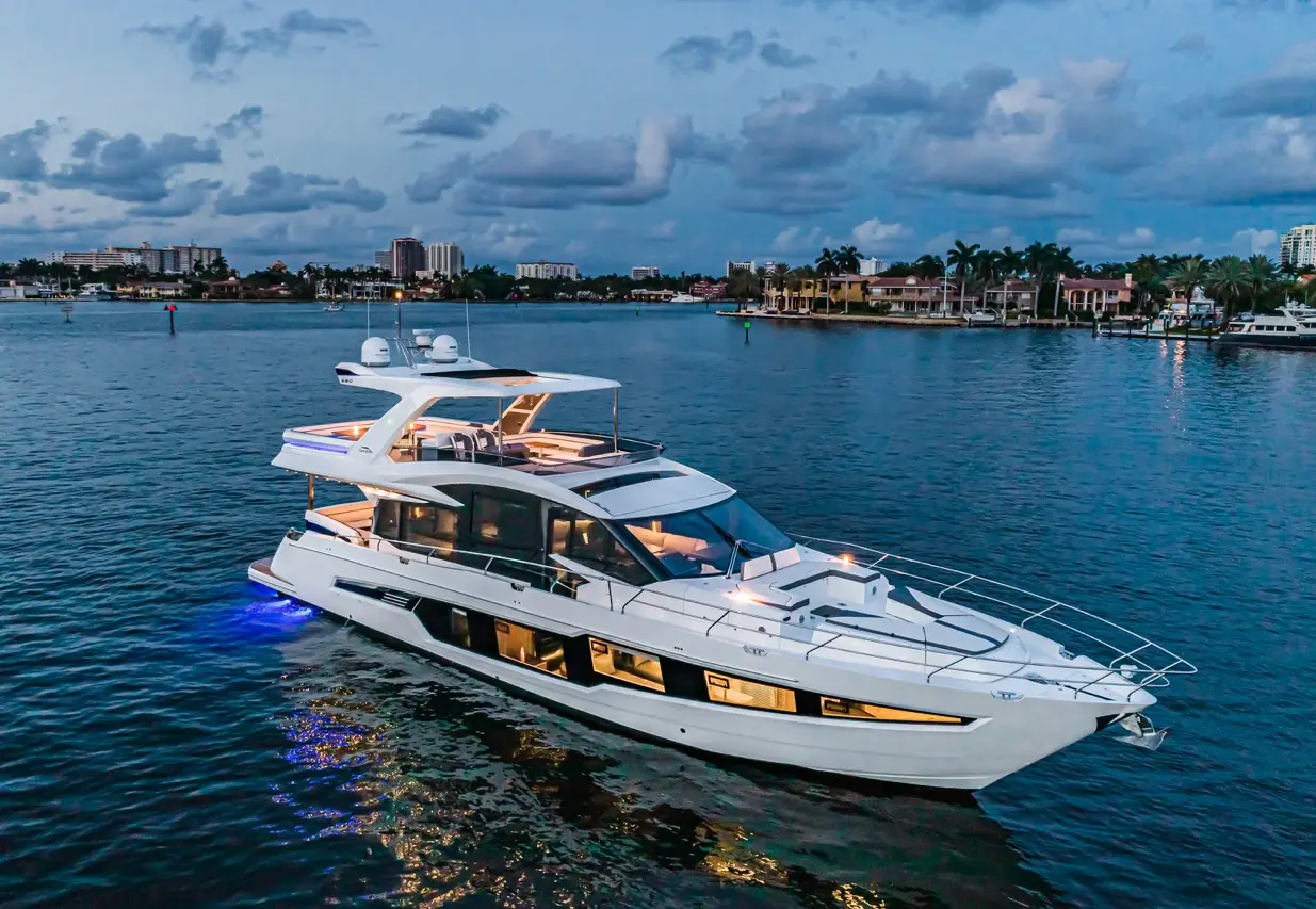 Luxury yacht cruising on calm waters at dusk, showcasing modern design and illuminated features against a vibrant skyline.