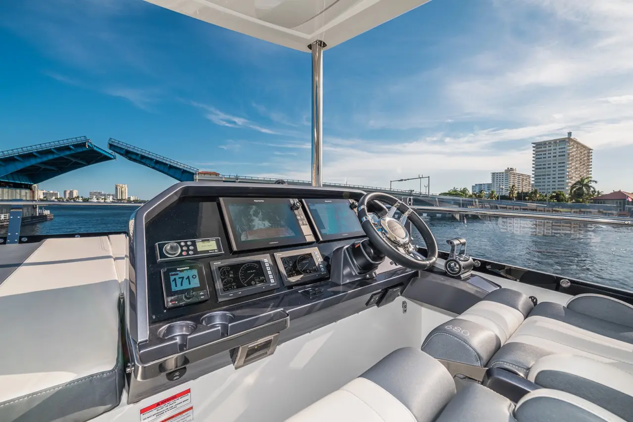 Boat dashboard with steering wheel, displays showing speed and navigation, overlooking a bridge and city skyline.