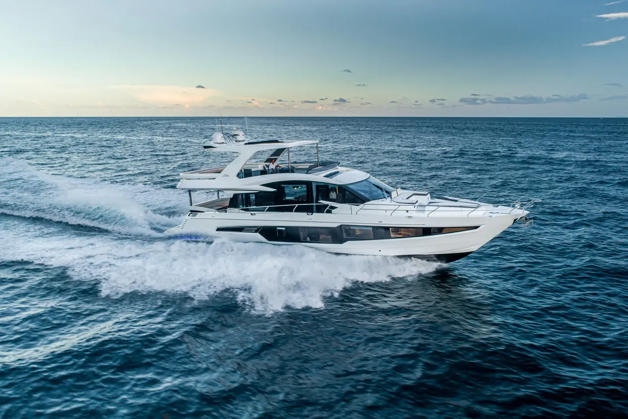A sleek white motor yacht speeds through the waves on open water, under a cloudy sky at sunset.