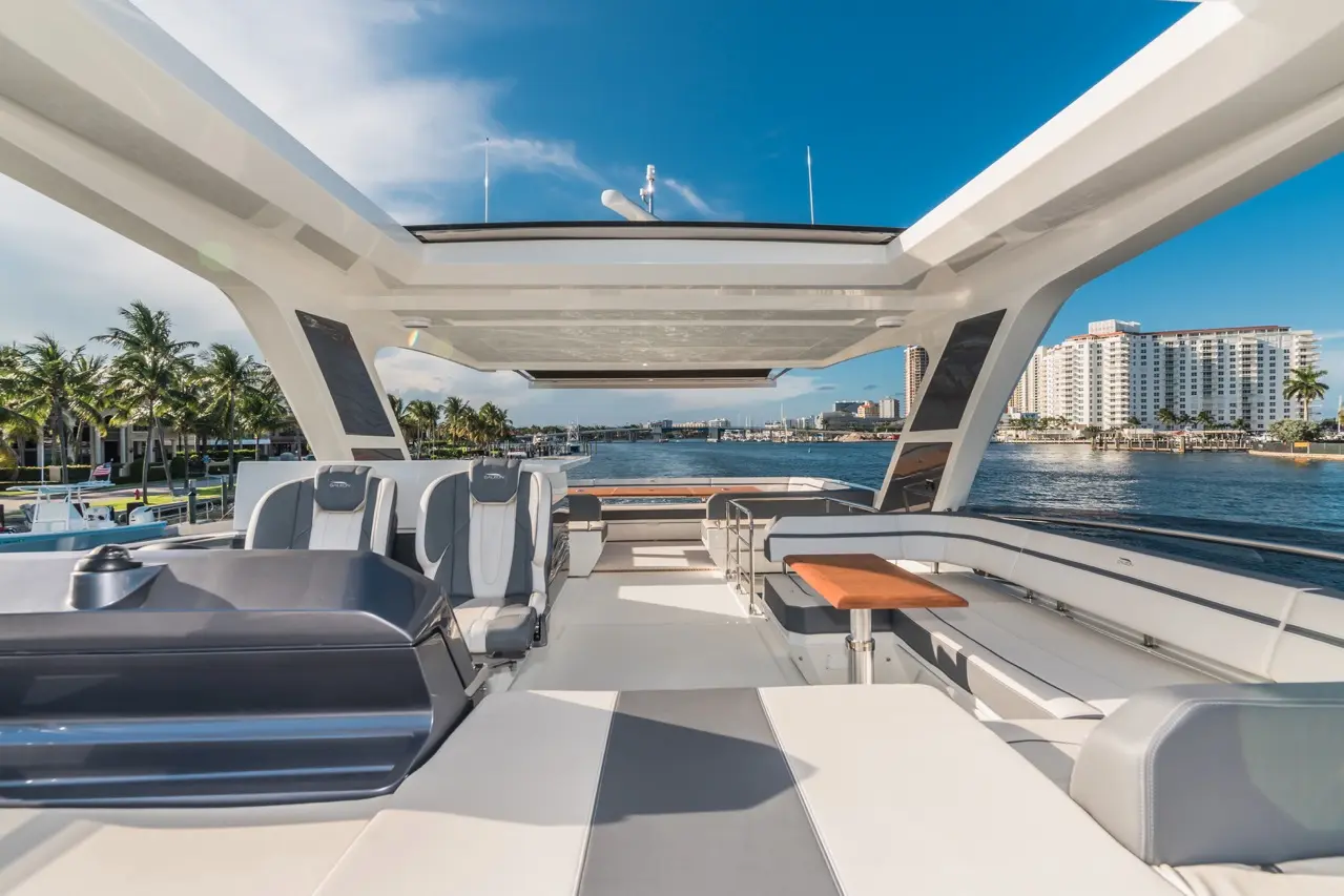 Luxury yacht deck with modern seating, wooden table, and panoramic views of the marina and city skyline under clear blue skies.