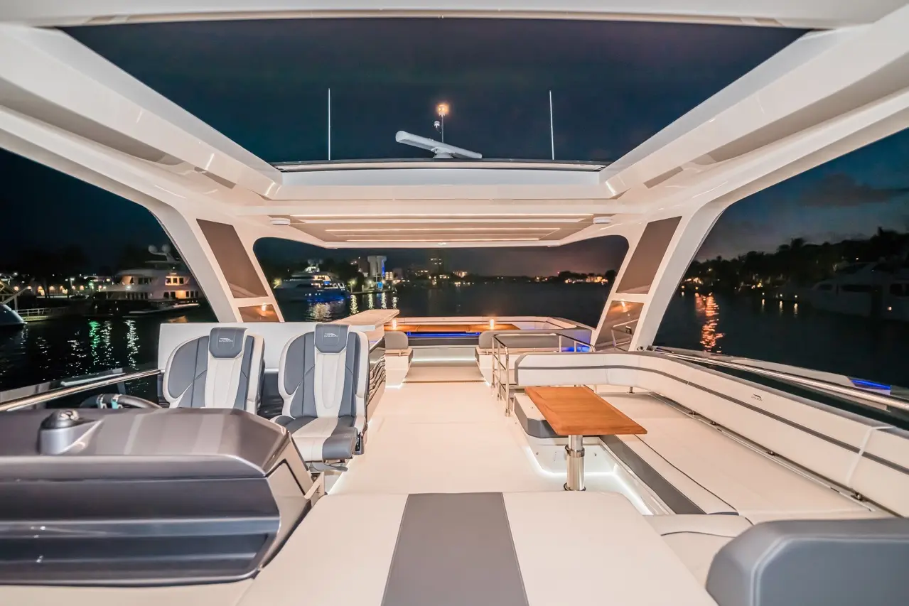 Luxurious yacht interior at night with modern seating, dining area, and scenic waterfront view. Brightly illuminated ambiance.
