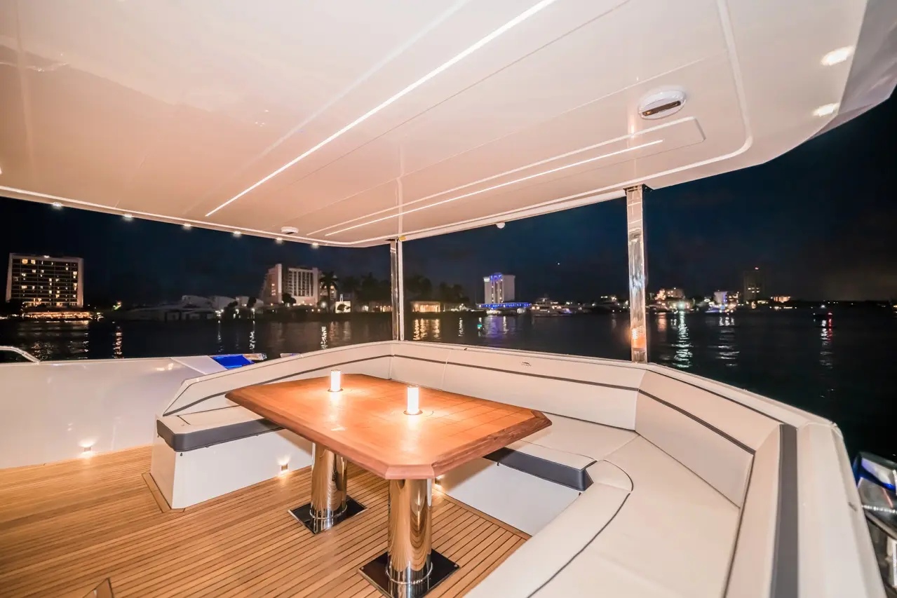 Luxury yacht interior featuring a wooden table with candles, illuminated at night, overlooking city lights on the water.
