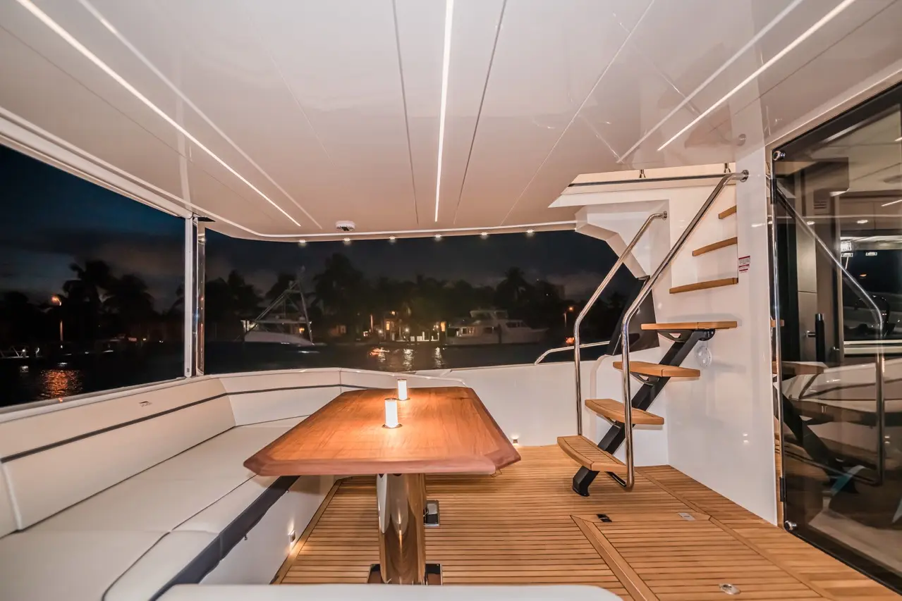 Interior of a luxury yacht at night, featuring a wooden dining table, seating, and spiral staircase, with ambient lighting.