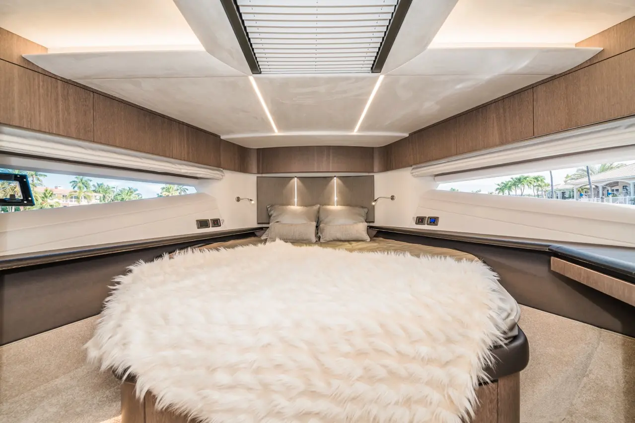 Luxurious boat interior featuring a rounded bed with a fluffy white throw, two silver pillows, and large windows with scenic views.