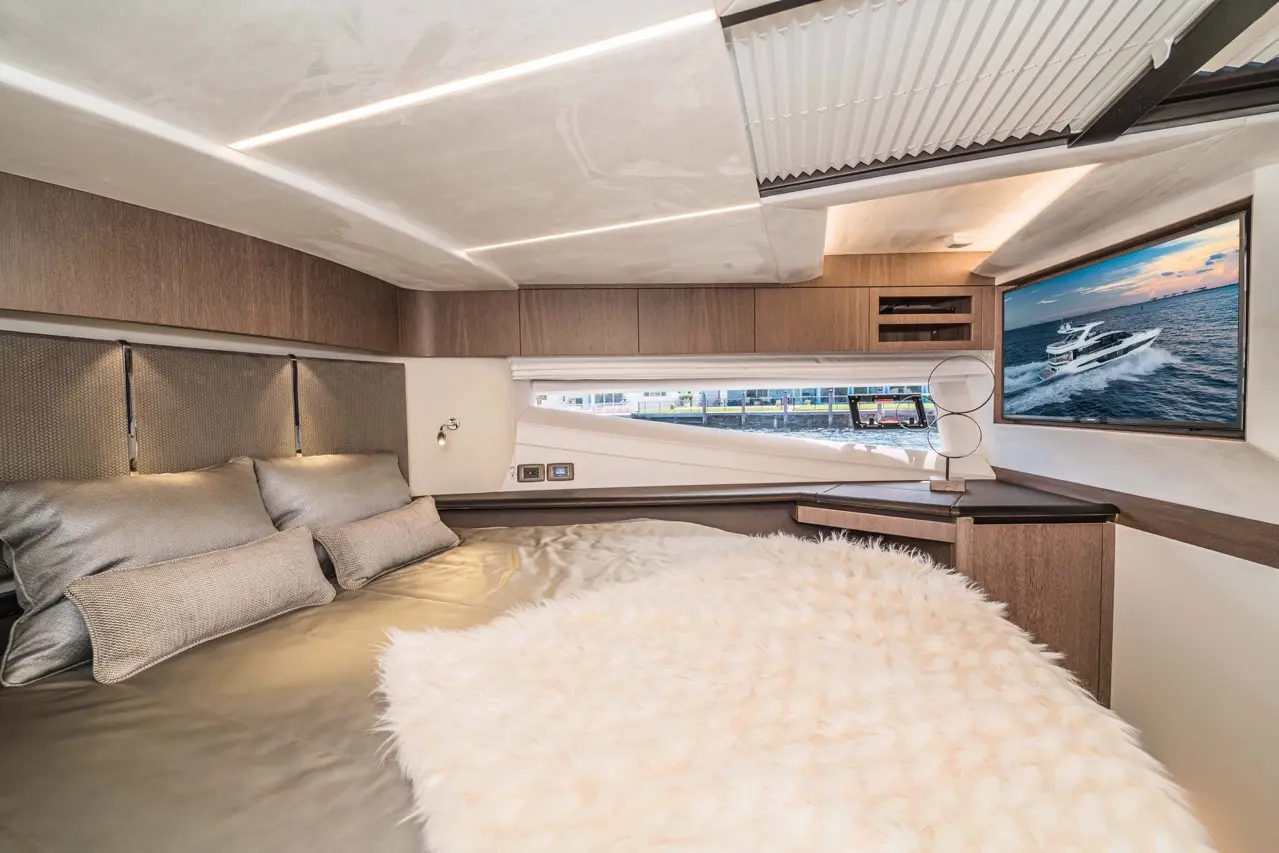 Modern boat interior featuring a luxurious bed, decorative pillows, and a large TV showcasing a yacht on the water.