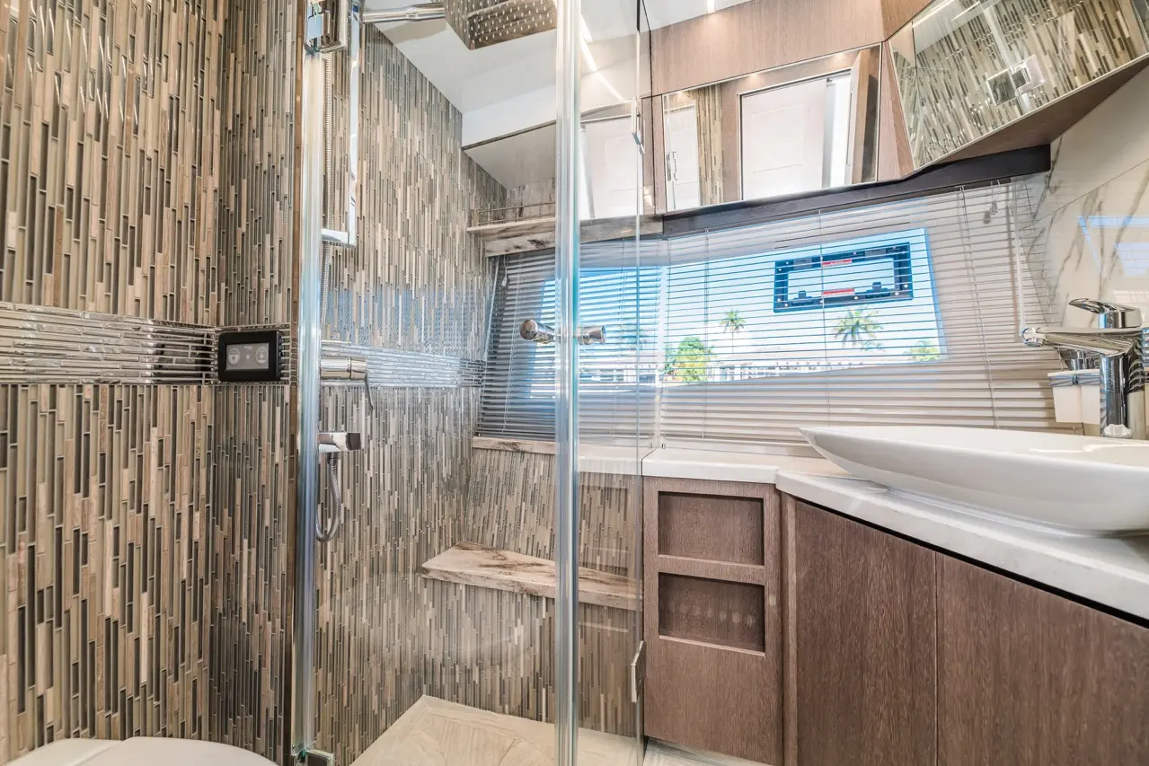 Modern bathroom featuring a glass shower, patterned tiles, wooden cabinetry, and a stylish sink with natural light streaming in.