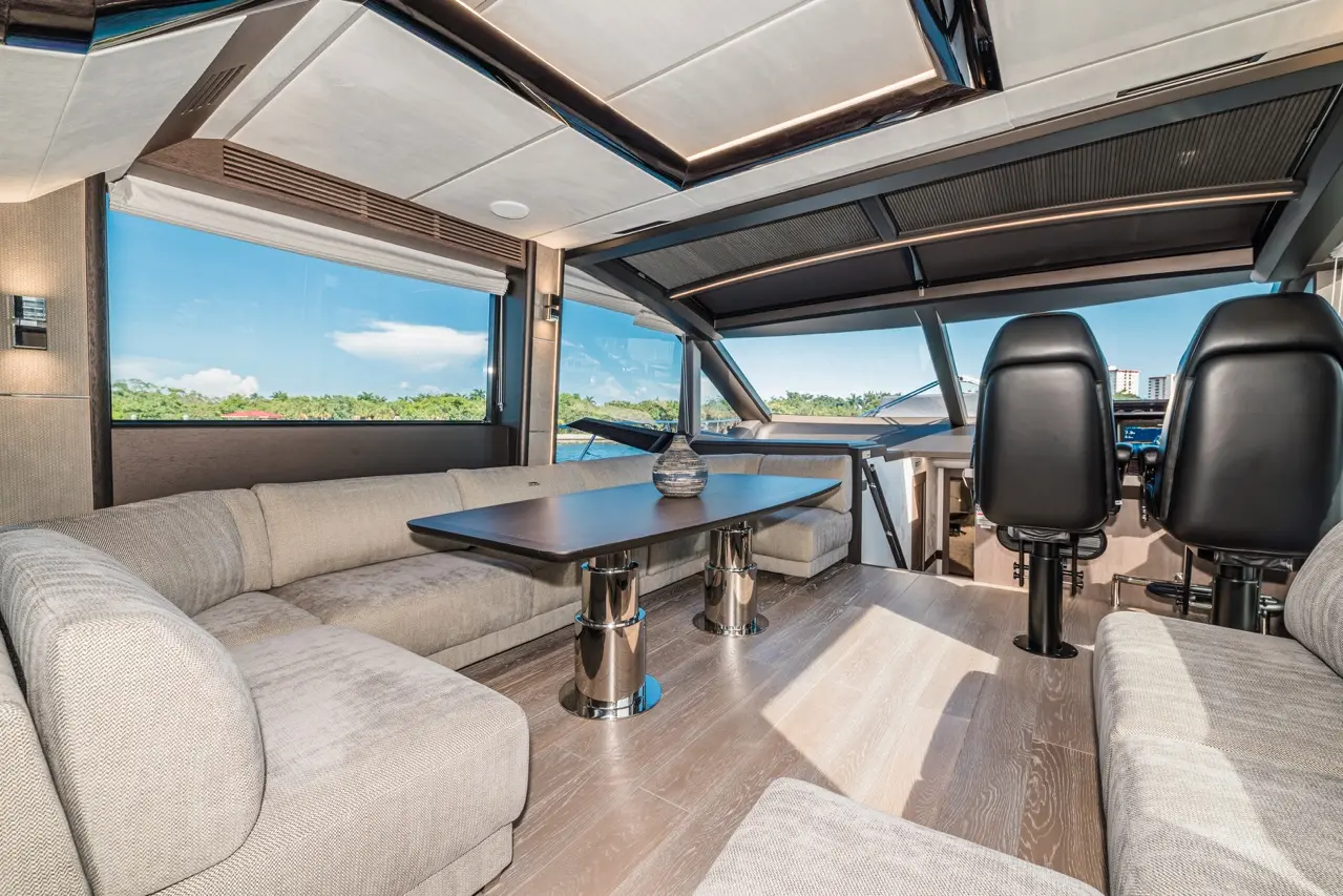 Stylish yacht interior featuring a lounge area with a large table, plush sofas, and panoramic windows for scenic views.