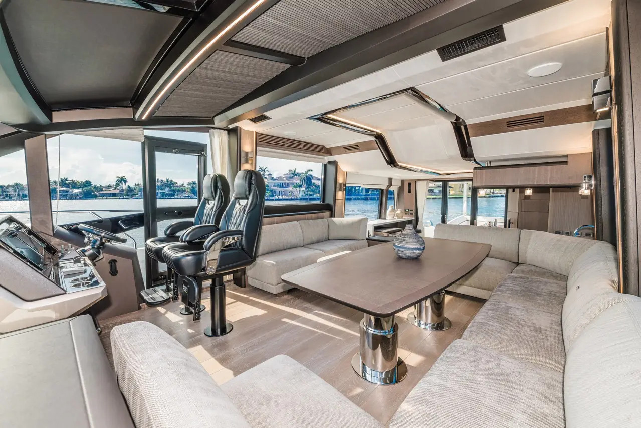 Luxurious yacht interior with leather captain chairs, a plush sofa, and a table, featuring large windows with water views.