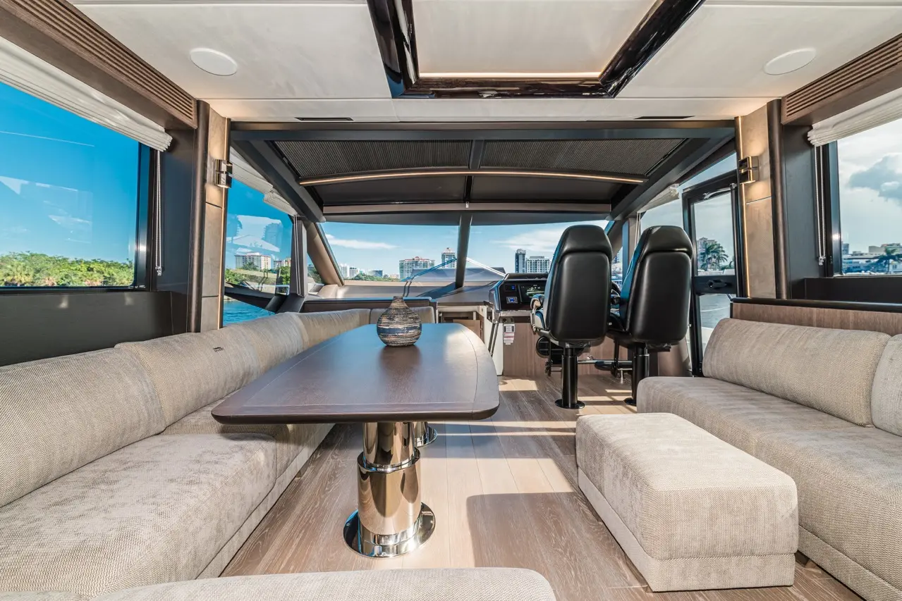 Spacious yacht interior featuring a coffee table, plush seating, and a helm with panoramic windows and skyline views.