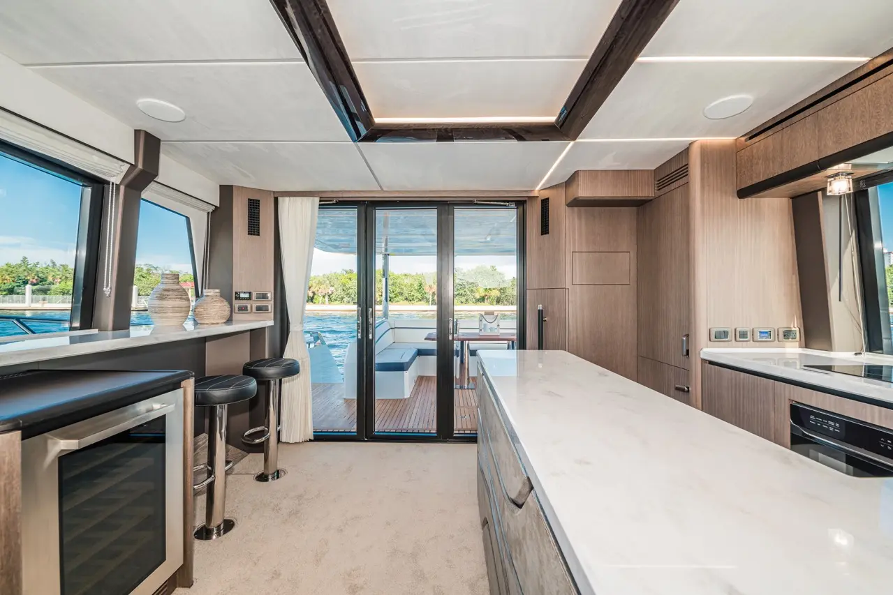 Modern yacht interior featuring a sleek kitchen with marble countertops, bar stools, and large glass doors overlooking the water.